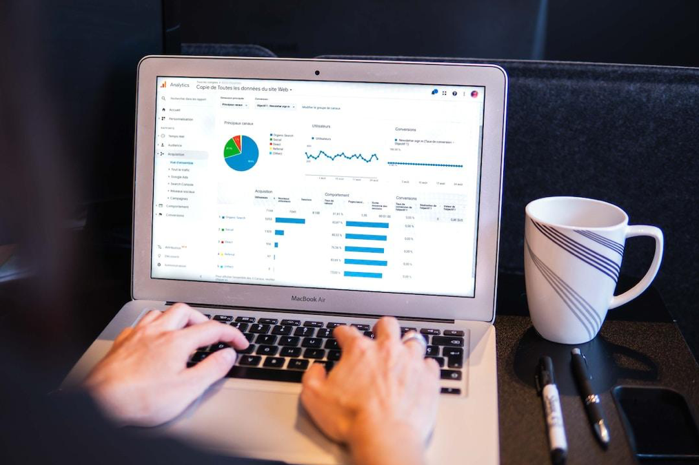 A performance data analytics dashboard on a laptop screen someone is typing on, with a mug and pens beside them.